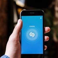 Hand holding smartphone with Shazam app open, displaying "Listening".