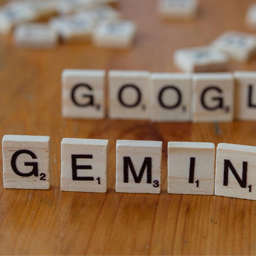 Scrabble tiles spelling "GEMINI" in front of blurred "GOOGLE".